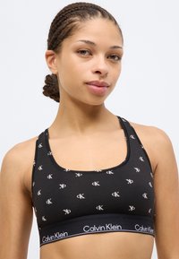 Μαύρο αθλητικό σουτιέν με λευκό μοτίβο λογότυπου CK, φαρδιά ελαστική ταινία με την επιγραφή «Calvin Klein», λαιμόκοψη scoop και μαλακό βαμβακερό υλικό.