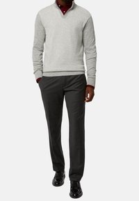 Maglione grigio a maglia con scollo a V e maniche lunghe, abbinato a pantaloni grigio scuro; scarpe nere; dettagli a strati visibili, materiale testurizzato.