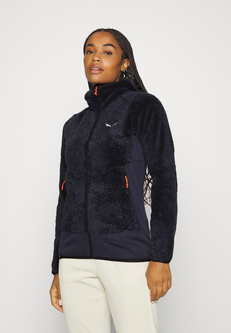 Navy blue fleece jacket with a high collar, textured body, contrasting orange zipper pulls, and smooth navy side panels.