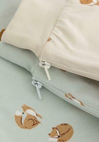 Deux housses de coussin : l'une beige avec des motifs de renard, l'autre vert clair avec des designs similaires. Les deux présentent des zips blancs et une texture de tissu douce.