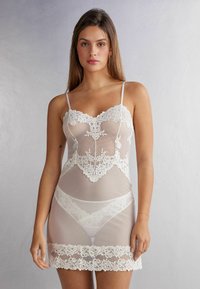 Witte kant babydoll nachtjapon met een aansluitende bodice met bloemenpatronen, dunne bandjes en doorschijnende stof. Kanten rand accentueert de zoom en de halslijn.