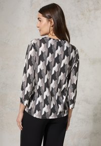 Driekwart mouwen top in een monochrome zigzagpatroon, met schakeringen van grijs en wit, en een zachte, gladde textuur.