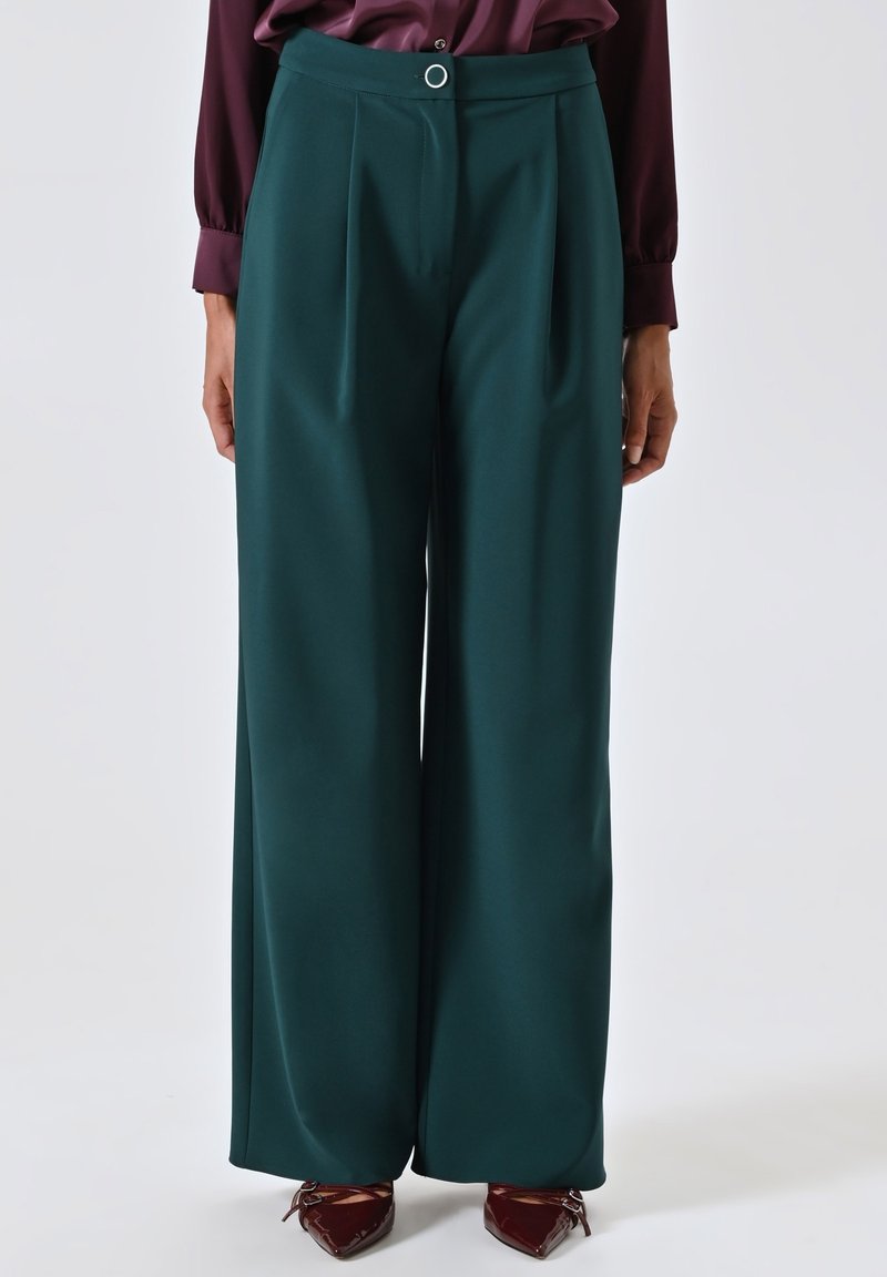 Pantaloni a gamba larga in tessuto blu scuro con una texture liscia, caratterizzati da plissettature frontali e una chiusura con bottone rotondo in vita.