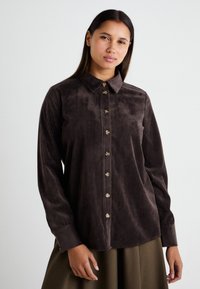 Bruine corduroy overhemden met een kraag, een knoopsluiting aan de voorkant en lange mouwen, met een verticale ribbelstructuur.