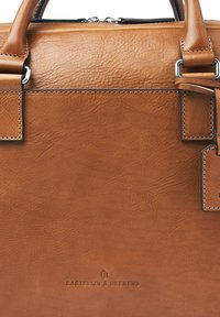 Tan leather briefcase with visible stitching, silver hardware, and Castelin & Beerens embossed logo on front panel.