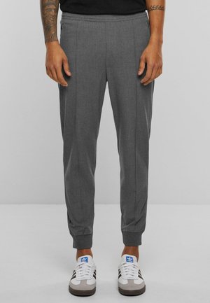 Graue taperte Jogginghosen mit Seitennähten, elastischem Bund und Knöchelbündchen, kombiniert mit weißen Sneakers mit dunklen Streifen.