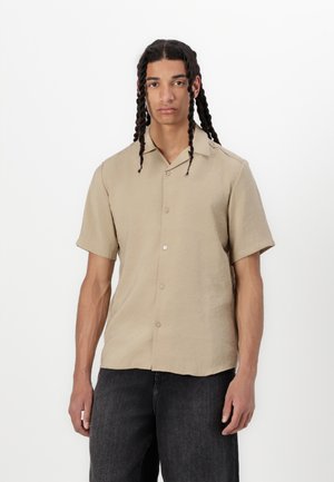Beige short-sleeve button-up shirt made from lightweight fabric, featuring a classic collar and a relaxed fit, paired with dark denim jeans.