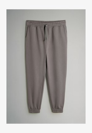 Pelēkās sporta bikses ar elastīgu jostu un regulējamu auklu. Iezīmē sānu kabatas un sašaurinātus kaklus pie potītēm. Gluda tekstūra.