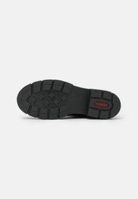 Suela de zapato de goma negra con un patrón de tacón multidireccional y logo de "rieker" en rojo. Bordes gruesos y texturizados para mayor durabilidad.
