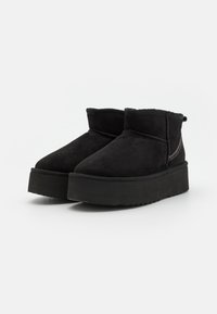 Botas negras hasta el tobillo de ante, con una suela de plataforma gruesa, punta redondeada y un detalle de cremallera en el costado. Textura suave y diseño minimalista.
