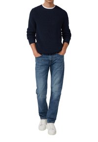 Navyblau gerippter Pullover mit Rundhalsausschnitt, kombiniert mit hellblauen Jeans. Weiße Sneakers runden den Look ab und betonen den lässigen Stil.