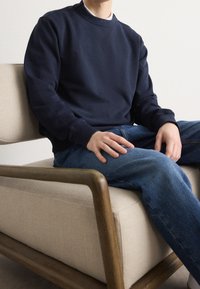 Tmavě námořnická mikina s kulatým výstřihem a žebrovanými manžetami, doplněná modrými džínami. Látka vypadá hladká a měkká.