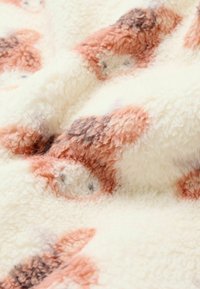 Flauschige Decke in Creme mit weicher, strukturierten Oberfläche. Enthält orangefarbene und braune abstrakte Muster. Gemütlicher, plüschiger Stoff.