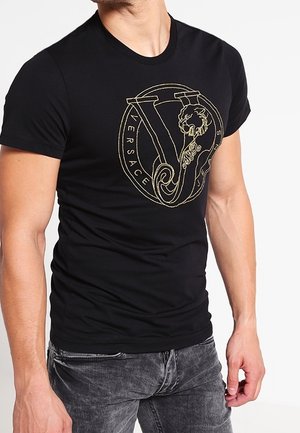T-shirt en coton noir avec un logo Versace en or, motif lion et design circulaire. Coupe ajustée avec des manches courtes.