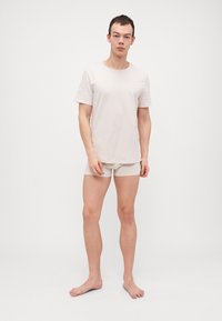 Beige Baumwoll-T-Shirt mit kurzen Ärmeln, kombiniert mit passenden beigen Shorts. Einfaches Design, weiche Textur, keine sichtbaren Muster oder Akzente.