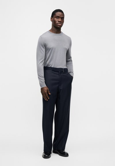 Chemise grise à manches longues avec une texture côtelée, associée à un pantalon bleu marine à fines rayures. Le pantalon est équipé d'une ceinture et présente une coupe classique.