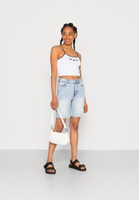 Top cropped branco com padrão de corações, calções de denime azul claro, sandálias pretas e uma pequena bolsa branca. Design minimalista.