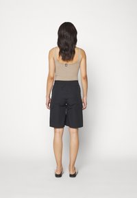 Svarta cargoshorts med elastisk midja och framfickor; kombinerat med en åtsittande beige linne. Modellen ses bakifrån.