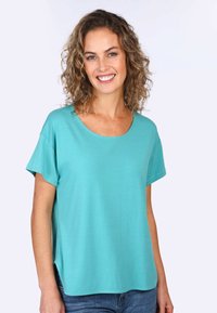 Türkises Kurzarm-T-Shirt mit lässiger Passform, rundem Ausschnitt und seitlichen Schlitzen. Weicher Stoff, kombiniert mit blauen Jeans.