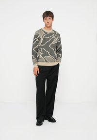 Gebreide trui met een golfpatroon in beige en zwart. Ronde hals, lange mouwen en geribbelde zoom. Gecombineerd met zwarte cropped broek met wijde pijpen.
