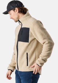 Fleece jacket in cream with a black zippered chest pocket and contrasting zippered side pockets. Features a high neck and elastic cuffs.