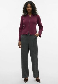 Bordeaux zip-up tröja med långa ärmar, kombinerad med grå rutiga vida byxor och spetsiga klackar. Slät textur, skräddarsydd passform.