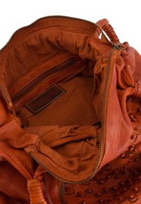 Braune Lederhandtasche mit strukturiertem Äußeren, Reißverschlussverschluss und gefüttertem Innenraum, der ein Reißverschlussfach und ein Markenetikett umfasst.