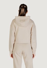 Felpa beige cropped con cappuccio foderato, polsini a coste e spalle morbide, realizzata in morbido tessuto misto cotone.