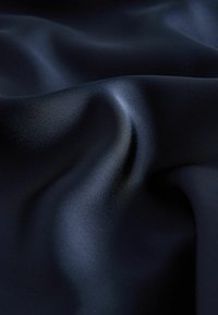 Tumši zilas samta audums ar gludu, spīdīgu tekstūru; šis audums ir ar mīkstiem krokām un viļņiem, radot plūstošu izskatu.