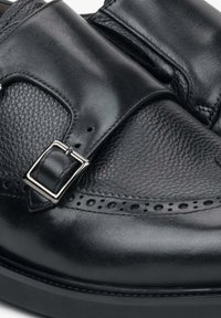 Czarne skórzane buty wizytowe z fakturowanym wykończeniem, z paskiem na klamrę, detalami w stylu brogue oraz gładkimi akcentami na nosku i boku.