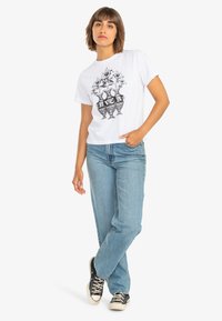 White cotton t-shirt featuring a black floral graphic print. Worn with light blue relaxed-fit denim jeans and black sneakers.