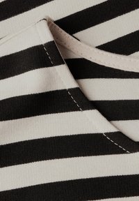 Czarna i kremowa tkanina w paski o miękkiej fakturze i widocznych szwach. Projekt cechuje się poziomymi paskami i okrągłym dekoltem.