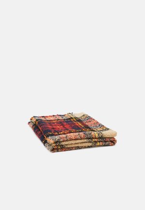 Couverture en laine pliée avec un motif à carreaux rouge, bleu marine, beige et jaune sur fond blanc.