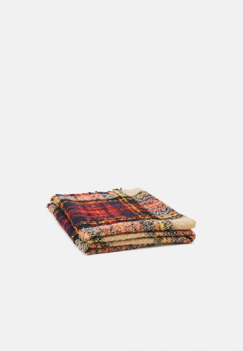 Couverture en laine pliée avec un motif à carreaux rouge, bleu marine, beige et jaune sur fond blanc.