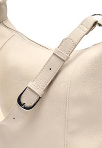 Borsa in pelle beige con superficie testurizzata e una larga tracolla regolabile con fibbia d'argento. Scomparto con zip visibile.