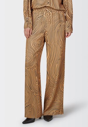 Wide-leg trousers in a tan color, featuring a black wave pattern. Made from soft fabric with an elastic waistband and drawstring detail.