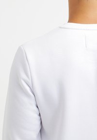 Weißes Baumwoll-Sweatshirt mit glatter Textur, runder Ausschnitt und einem einfachen, klaren Design. Die Rückseite zeigt eine nahtlose Konstruktion.