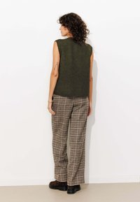 Haut en tricot sans manches de couleur vert olive associé à un pantalon large à carreaux marron, présentant une finition texturée et des bottes à plateforme noires.