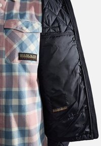 Pink og blå ternet skjorte med en forlommer sammen med en åben sort quiltet jakke, der viser en sort indvendig lomme.