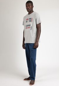 Camiseta de algodón gris con texto impreso en rojo y azul; combinada con pantalones oscuros azul marino; corte relajado; mangas cortas.
