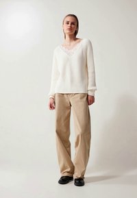 Witte geribbelde gebreide trui met een V-hals en kantafwerking, gecombineerd met losse beige broek en zwarte schoenen. Eenvoudig ontwerp, relaxte pasvorm.