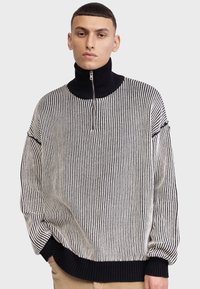 Pulover tricotat cu guler înalt cu fermoar, dungi verticale alb-negru și tiv și manșete cu textură ribbed.