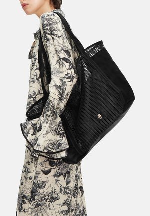 Mujer con un vestido floral blanco y negro que lleva un gran bolso de malla negro sobre el hombro.