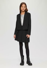Ensemble de blazer noir à rayures et de jupe plissée, associé à un haut argenté, des collants noirs et des bottes noires à semelle épaisse. Texture lisse, silhouette moderne.