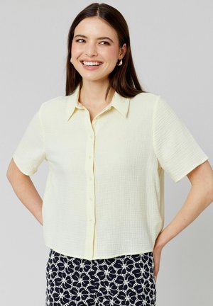Chemise jaune à manches courtes avec un tissu texturé. Présente un col classique et une coupe décontractée, assortie à un pantalon foncé à motifs.