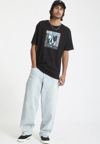 Sort T-shirt med et farverigt geometrisk logo, parret med lyseblå baggy jeans og sorte sneakers. Simpelt design med afslappet pasform.