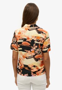 Camisa de manga corta con un estampado floral y geométrico en tonos naranjas, rosas y negros; tela ligera con un corte relajado.