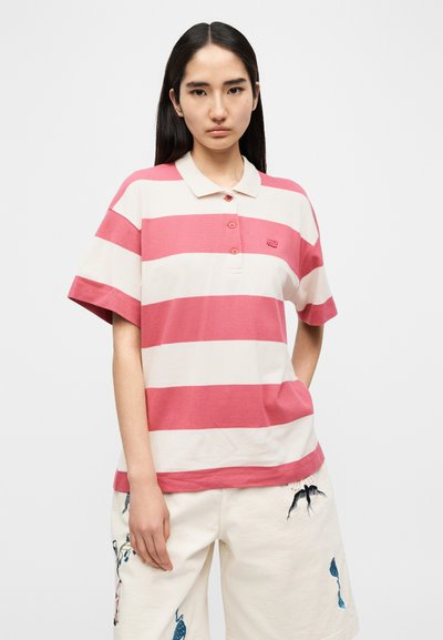 Polo rayé rose et crème avec col, patte de boutonnage et petit logo. Associé à un short blanc avec des détails brodés.