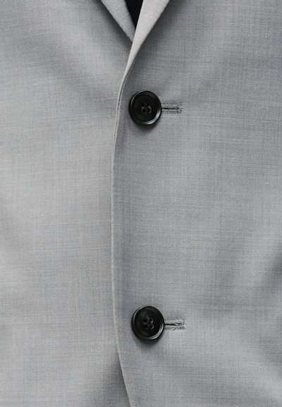 Ανοιχτό γκρι σακάκι με δύο μαύρα κουμπιά κουμπωμένα, εμφανίζοντας κουμπότρυπες και μέρος της πέτου.