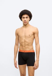 Μαύρα βαμβακερά μποξέρ με πορτοκαλί ελαστική μέση που φέρει το κείμενο "TOMMY HILFIGER". Ομαλή υφή και εφαρμοστή σχεδίαση.